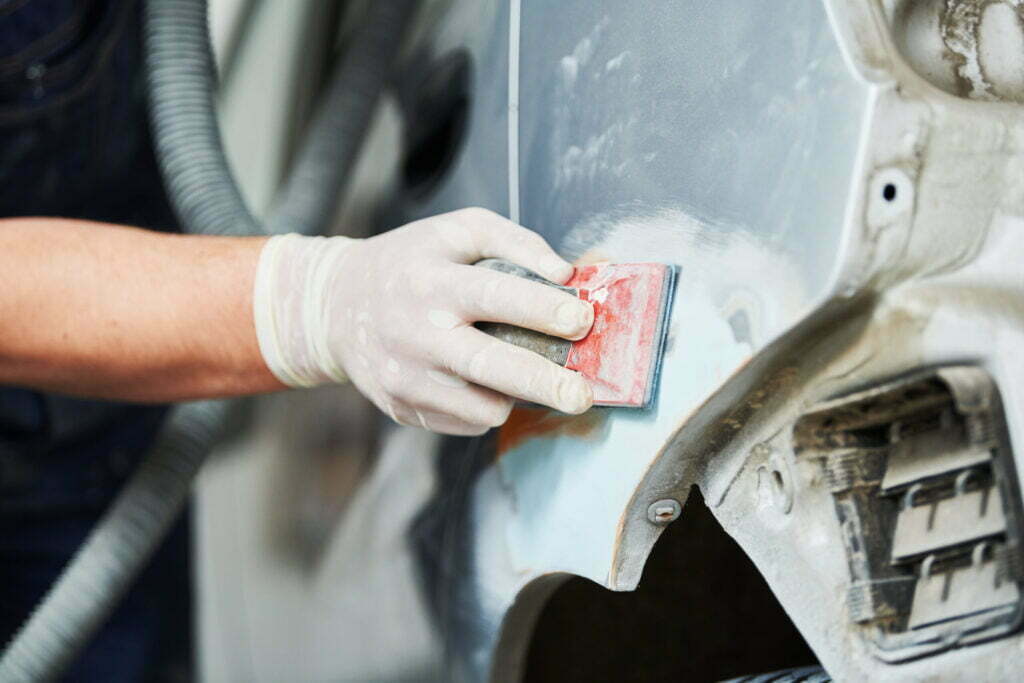 Auto body repairs. Repairman mechanic worker plastering and sanding automobile car body by plaster in garage workshop