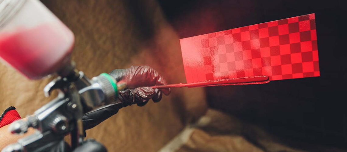A spray gun in the master s hands is aimed at a test plate and sprays paint in a tinting hood